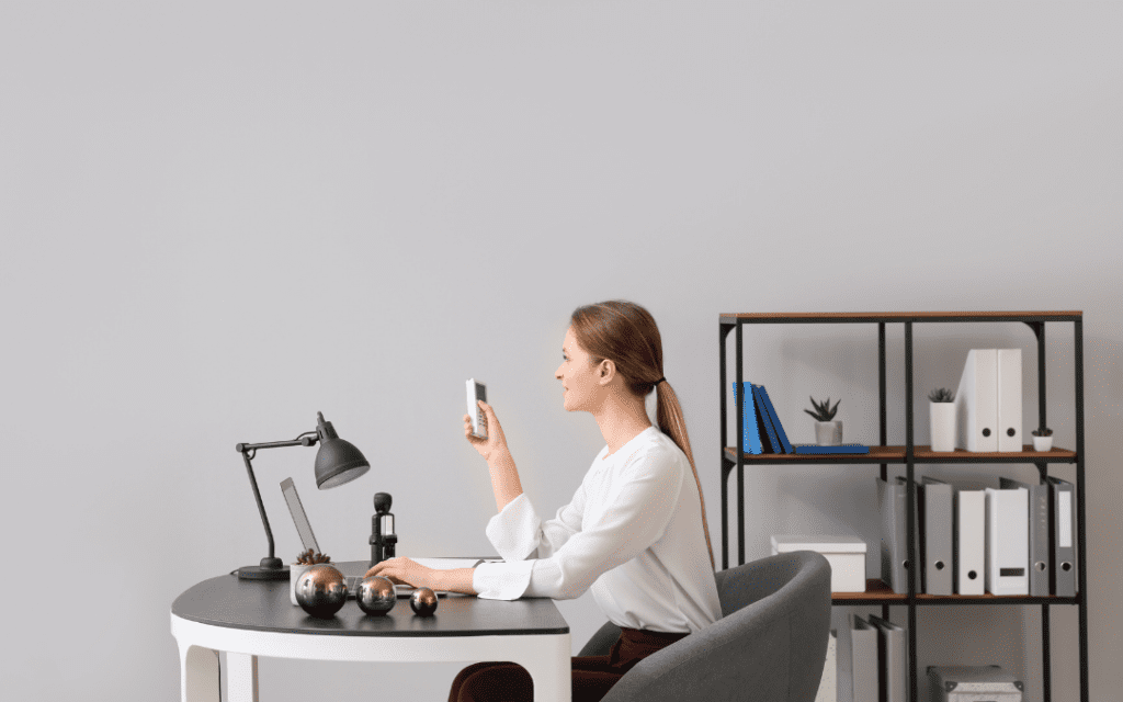 woman holding aircon remote and working on laptop